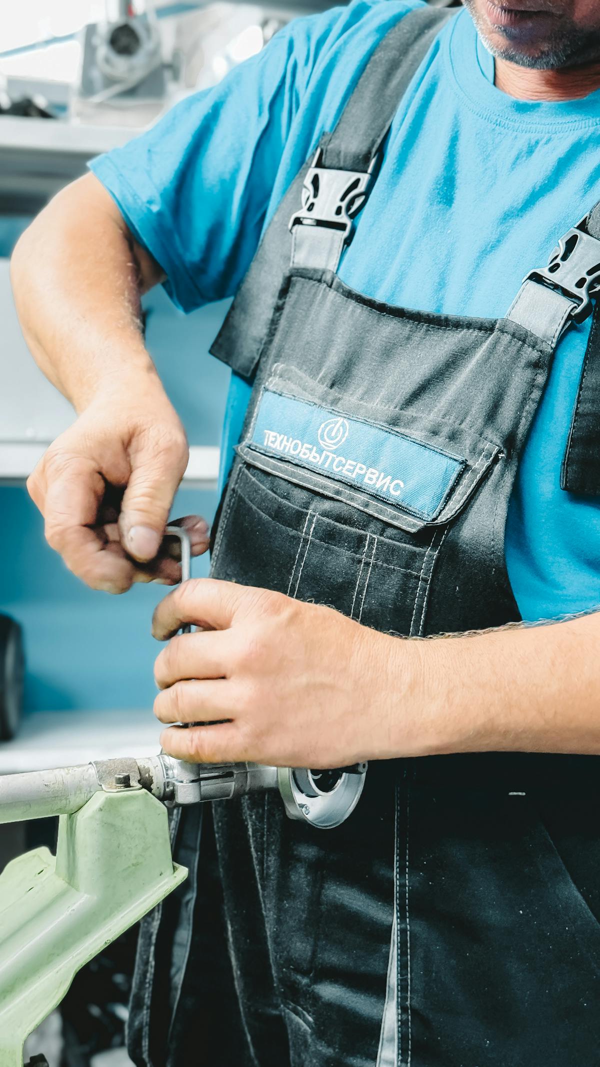 A plumber in a blue uniform tightening a pipe joint with a wrench